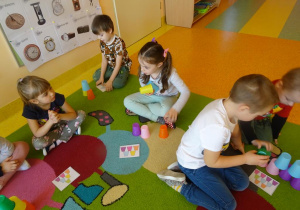 Dzieci układają wieże z kubeczków według wzoru na kartce.